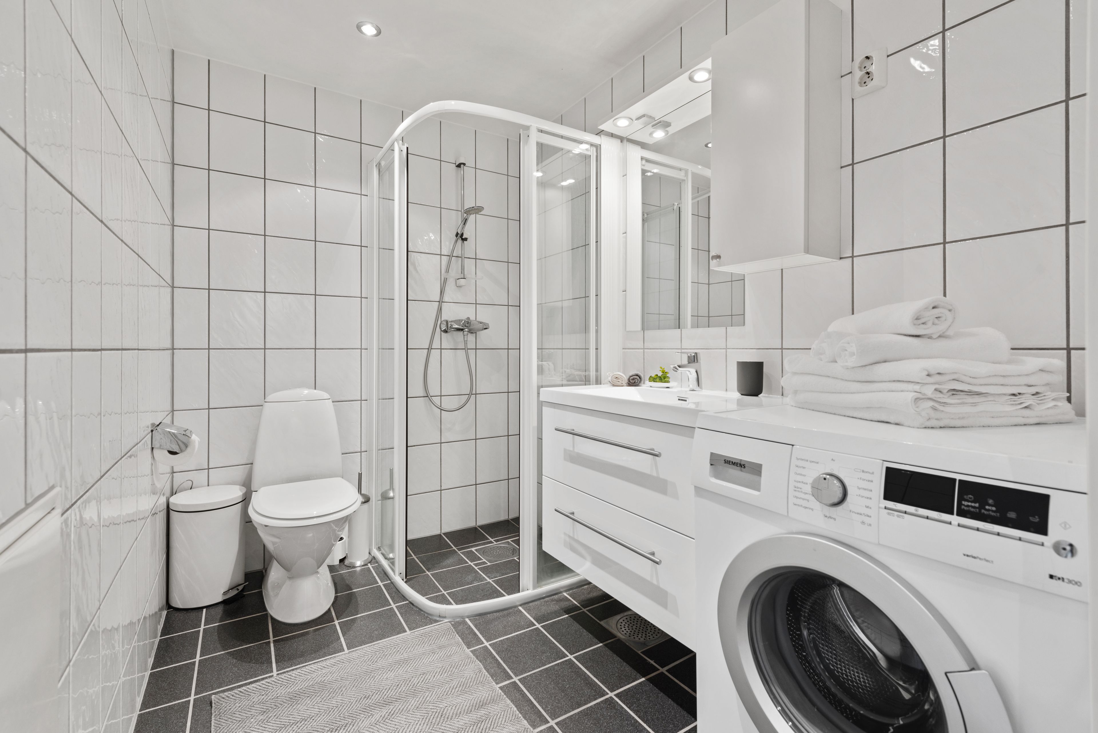 A modern bathroom with a shower, toilet, and a washing machine.