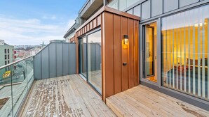 A modern hotel balcony with a wooden deck, large windows, and a glass railing. - Bjørvika Apartments, Solsiden Area, Trondheim city center (Trondheim)
