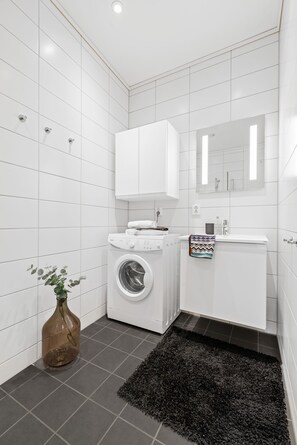 A modern bathroom with white tiles, a washing machine, a sink, and a mirror. - Bjørvika Apartments, Solsiden Area, Trondheim city center (Trondheim)
