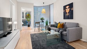 A modern living room with a grey sofa, a glass coffee table, a TV, and a painting on the wall. - Bjørvika Apartments, Solsiden Area, Trondheim city center (Trondheim)
