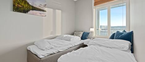 A bedroom with two beds, a window with blinds, a nightstand, and a painting on the wall.