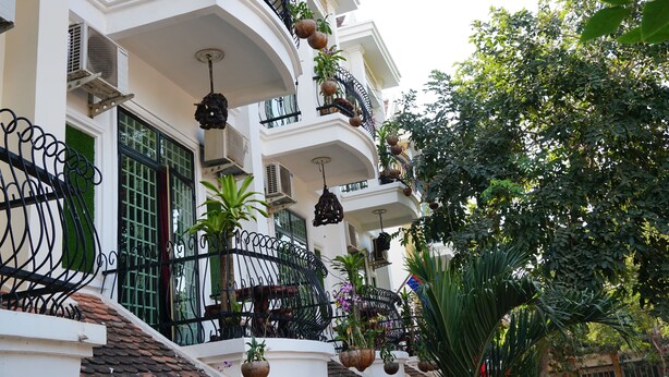 A multi-story building with balconies adorned with potted plants and hanging decorations. - WoodrootsBanteaychhmar (Siem Reap)