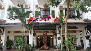 A hotel entrance with a central statue, multiple flags, and potted plants. - WoodrootsBanteaychhmar (Siem Reap)