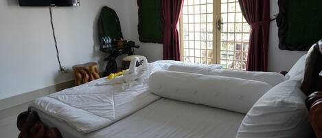 A neatly made bed with white linens, a flat-screen TV mounted on the wall, and a window with red curtains.