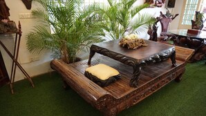 A wooden bench with a cushion, surrounded by green plants and a decorative table. - WoodrootsBanteaychhmar (Siem Reap)