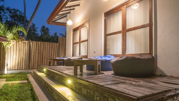 A patio area with a stone bench, a table, and a sofa. There are palm trees in the background. - Luaya Beach (Tangalle)
