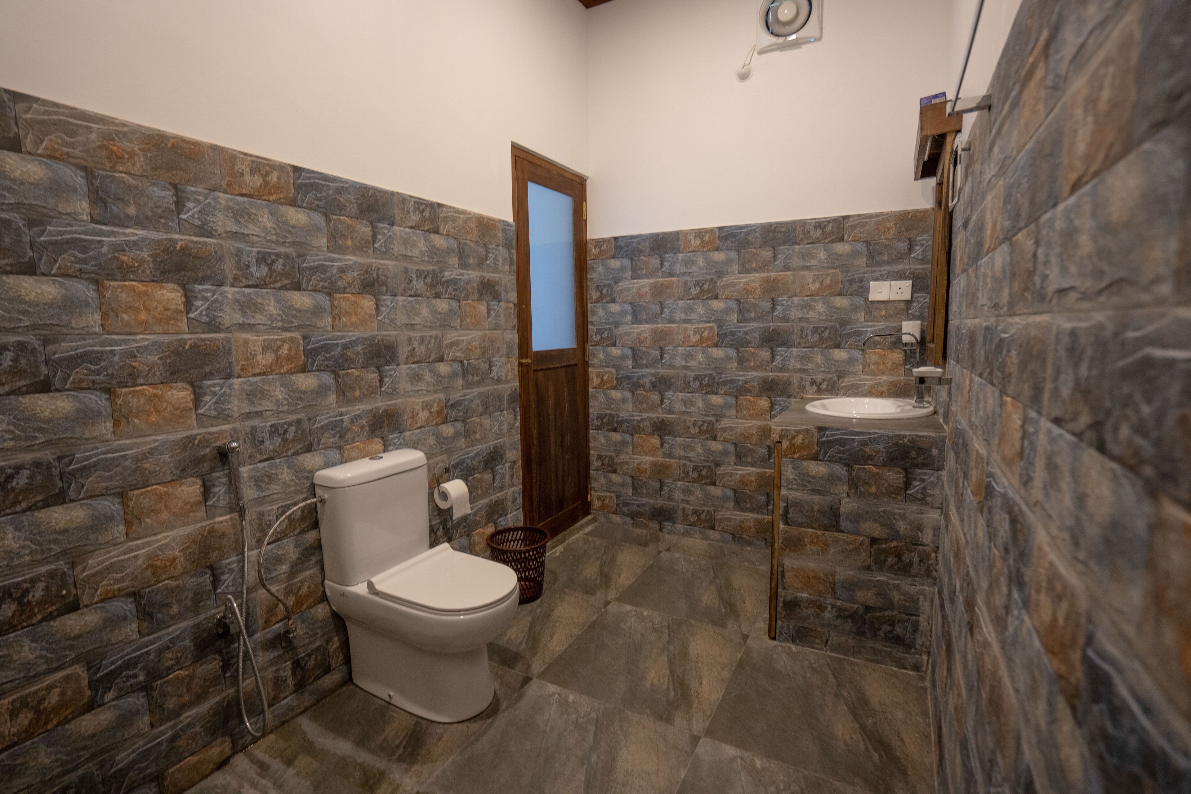 A bathroom with stone walls, a toilet, a sink, and a shower area.