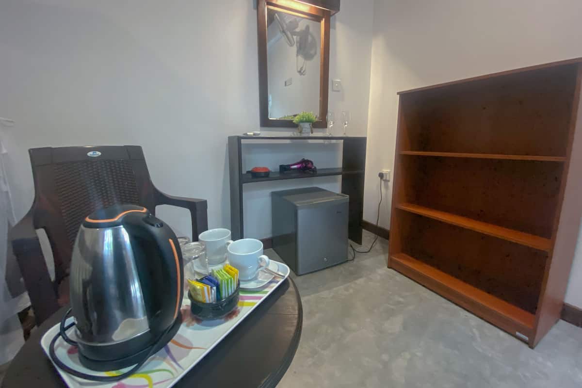 A room with a desk, a chair, a coffee maker, a tray with cups and a small plant, a shelf with decorative items, and a wooden cabinet.