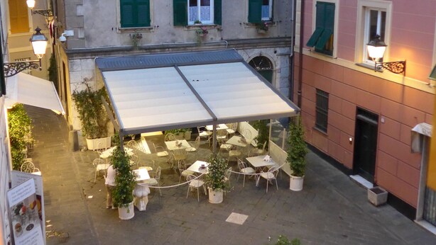 An outdoor cafe area with tables and chairs, surrounded by potted plants. - Giramondo Room and Breakfast (Rapallo)