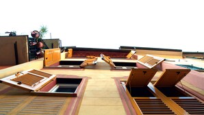 A rooftop terrace with multiple wooden louvers, a small seating area, and a potted plant. - Giramondo Room and Breakfast (Rapallo)