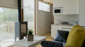 A modern kitchen with white cabinets, a microwave, and a sink. There is a dining area with a table and chairs, and a sofa with cushions. - Aloia Nature Alojamiento Forestal (Tui)