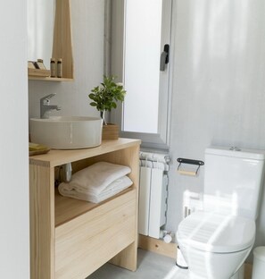 A modern bathroom with a white sink, wooden vanity, a potted plant, and a toilet.
