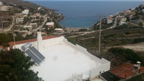A coastal town with a view of the sea. There are houses with red roofs and a white building with a flat roof. - Villa V (Lavreotiki)