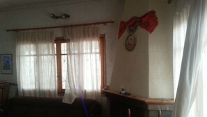 A living room with a sofa, a window with curtains, a wall clock, and a small table. - Villa V (Lavreotiki)