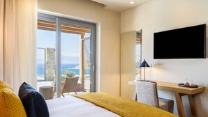 Habitación de hotel con cama, escritorio, televisión y balcón con vista al mar.
