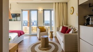 Una habitación de hotel moderna con cama, sofá y una mesa redonda de madera. Tiene un balcón con vistas a la ciudad.