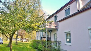 Ein zweistöckiges Gebäude mit Balkon, einem Auto auf der Auffahrt und einem Baum im Vordergrund.