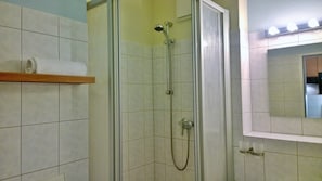 A shower with a glass door, a towel rack with a white towel, and a mirror with lights above it. - Ostsee Micro Ferienappartements (Ostseebad Dierhagen)