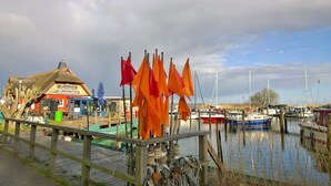 Eine Holzsteganlage mit Booten, ein Gebäude mit Strohdach und orangefarbenen Flaggen.