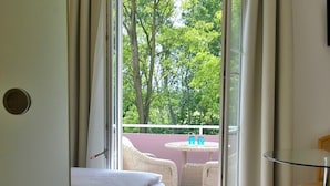 Ein Schlafzimmer mit Bett, Glastisch, Stuhl und Blick auf einen Balkon mit Tisch und Stühlen.