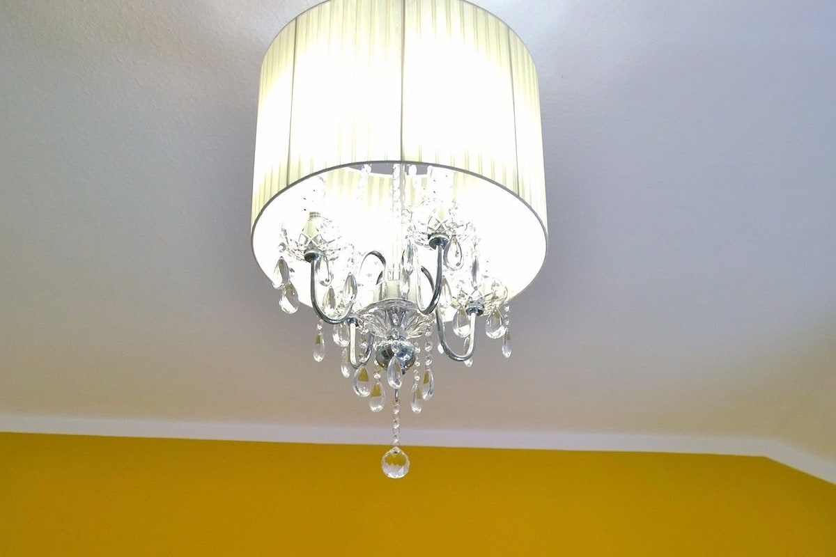 Cama doble con sábanas blancas, un candelabro y dos lámparas de noche en una habitación con paredes amarillas.