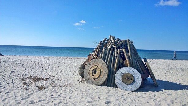 Ein Strand mit einem Holzstoß und zwei großen Rädern.