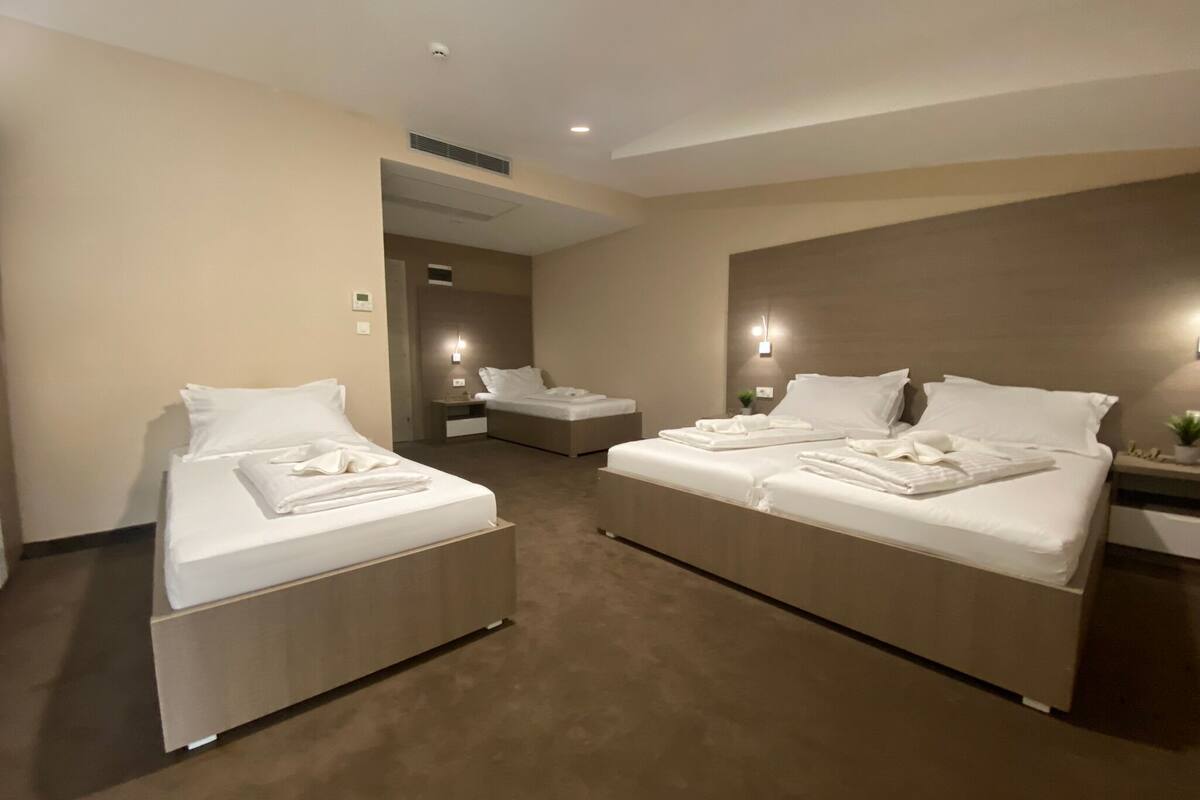A hotel room with two beds, a small seating area, and a door leading to another room.