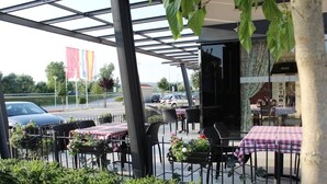 Un café al aire libre con mesas y sillas, rodeado por una valla de metal y follaje.