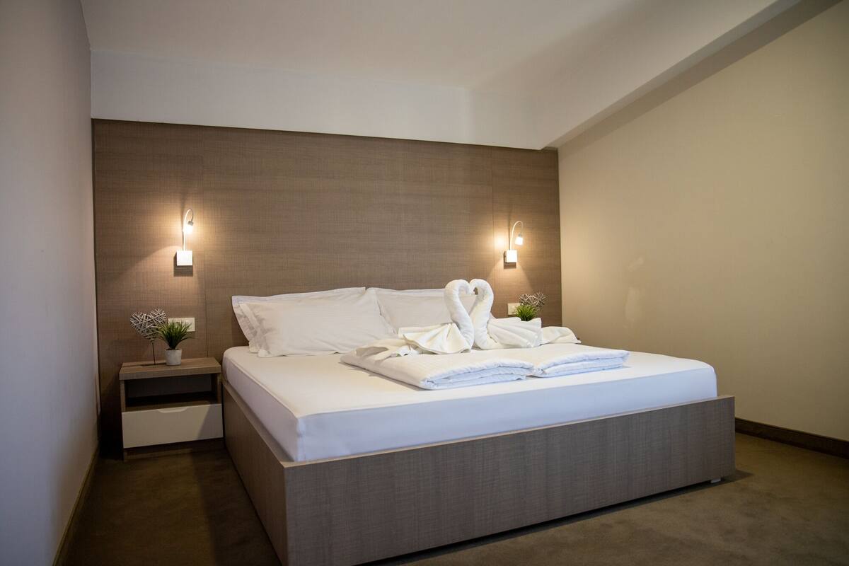 A modern hotel room with a large bed, two bedside tables, and wall-mounted lights.