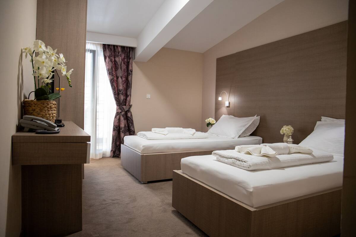 A hotel room with two beds, a desk with a telephone, and a vase of flowers.