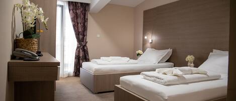 A hotel room with two beds, a desk with a telephone, and a vase of flowers.