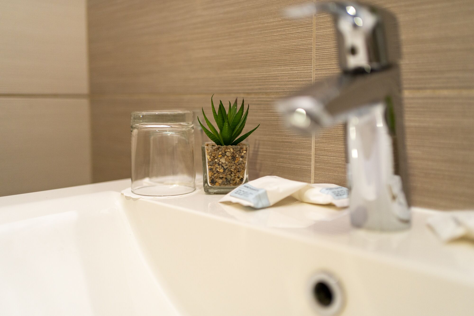 Un lavabo de salle de bain avec un bocal en verre transparent, une petite plante en pot et un robinet.