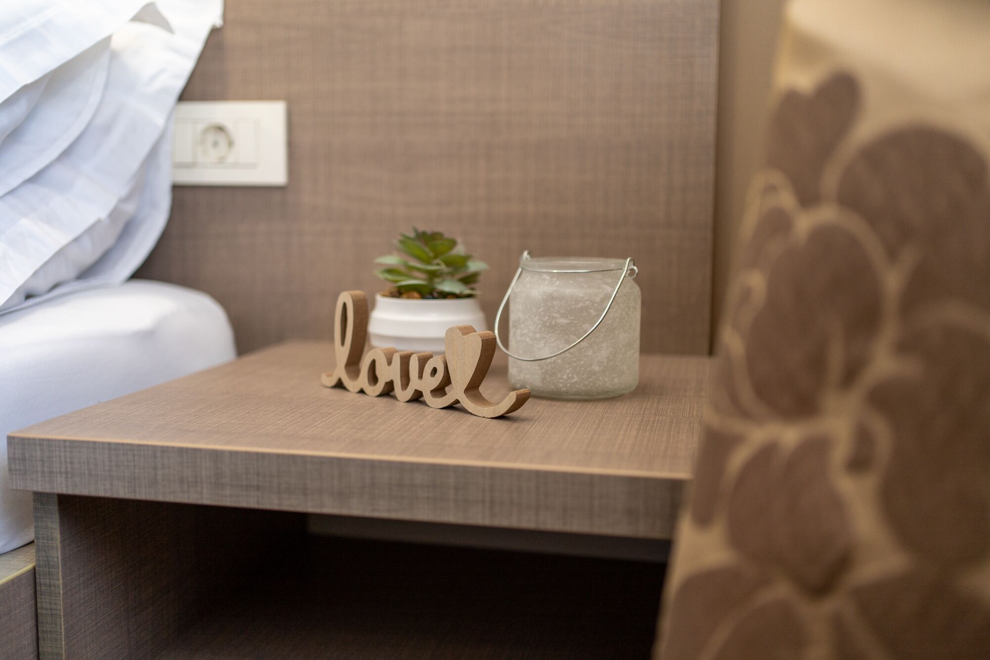 A bedside table with a small potted plant, a glass jar with a metal handle, and wooden letters spelling "love".