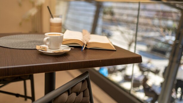 Una mesa con una taza de café, un libro y una pajita.