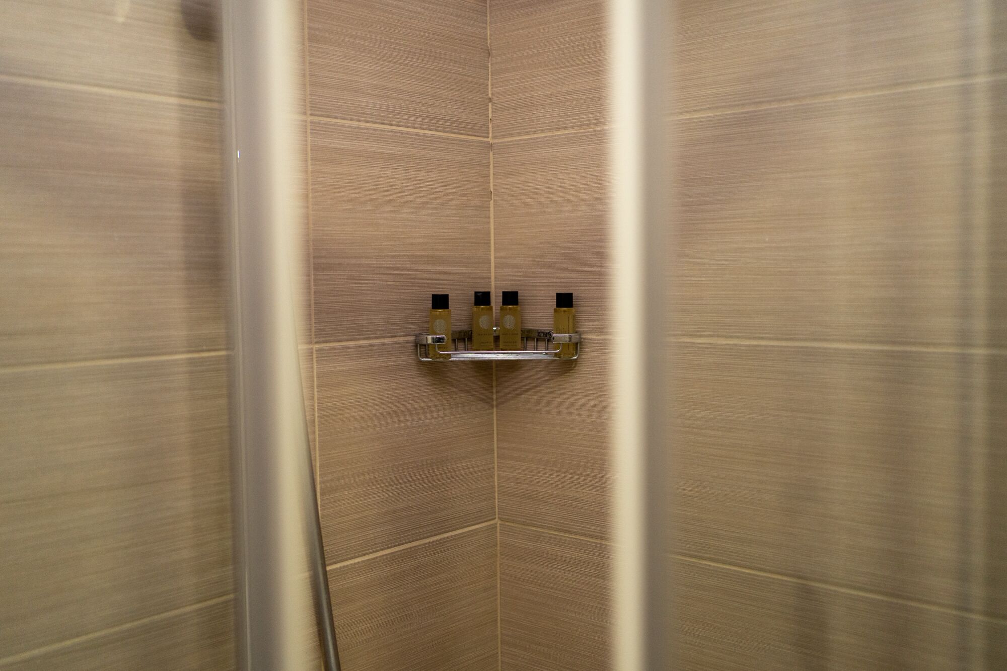A corner of a room with a tiled wall and a shelf with toiletries.