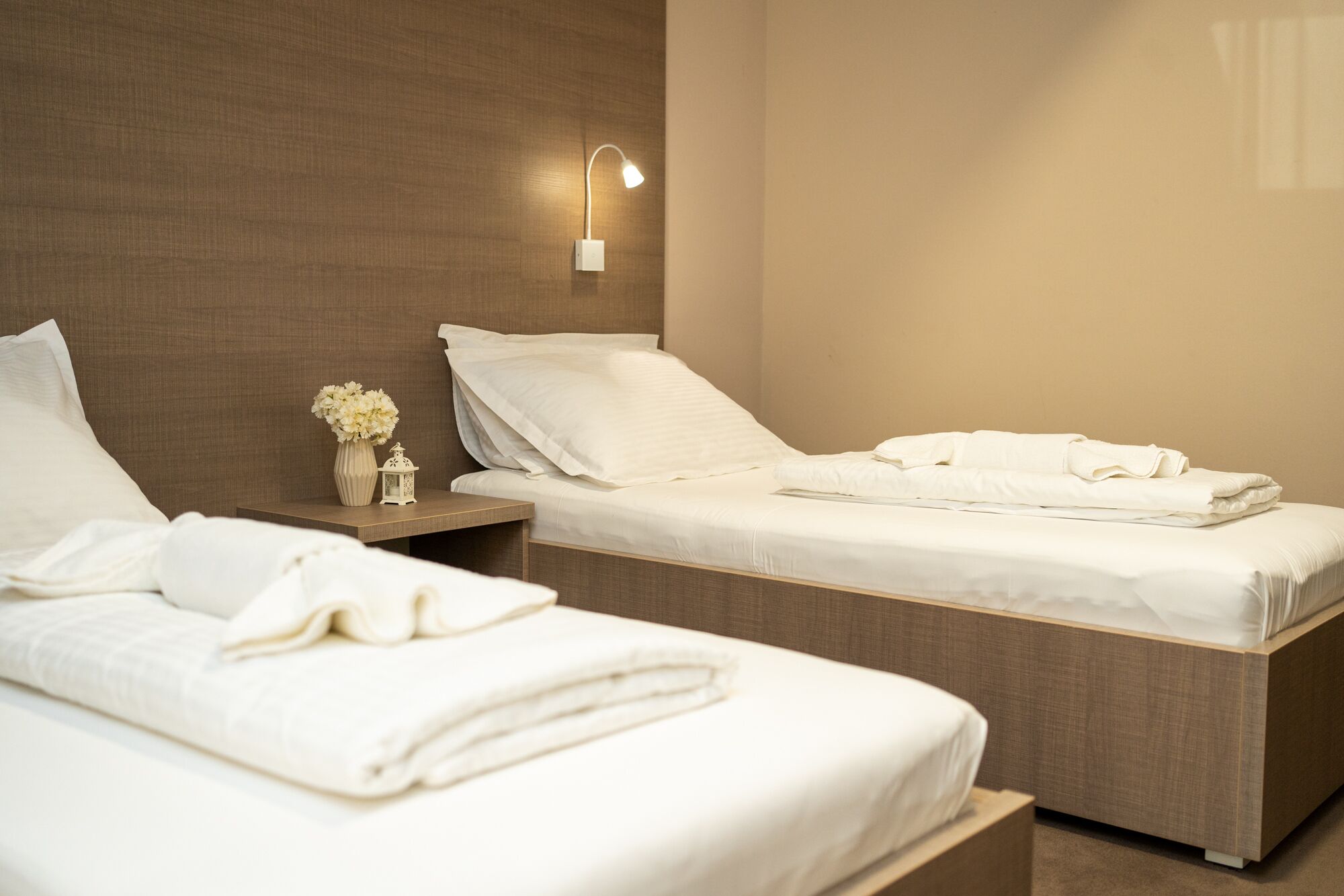 Ein Hotelzimmer mit zwei Betten, einem Nachttisch mit Blumenvase und einer Wandlampe.