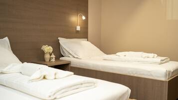 A hotel room with two beds, a nightstand with a vase of flowers, and a wall-mounted lamp.