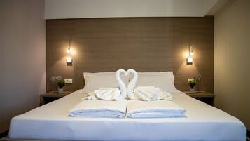 A neatly made bed with towels arranged in a heart shape, two wall-mounted lights, and small potted plants on bedside tables.
