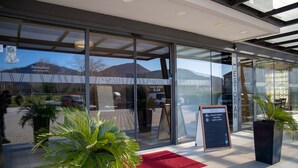 Una entrada de hotel moderna con puertas de vidrio, un mostrador de recepción y una alfombra roja que invita a entrar.
