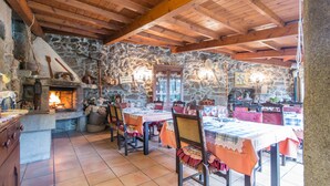Un comedor rústico con paredes de piedra, vigas de madera y una chimenea. Las mesas están dispuestas con manteles y sillas.