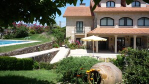 Una casa grande con piscina, un patio con sombrilla y un jardín con flores y una maceta decorativa grande.