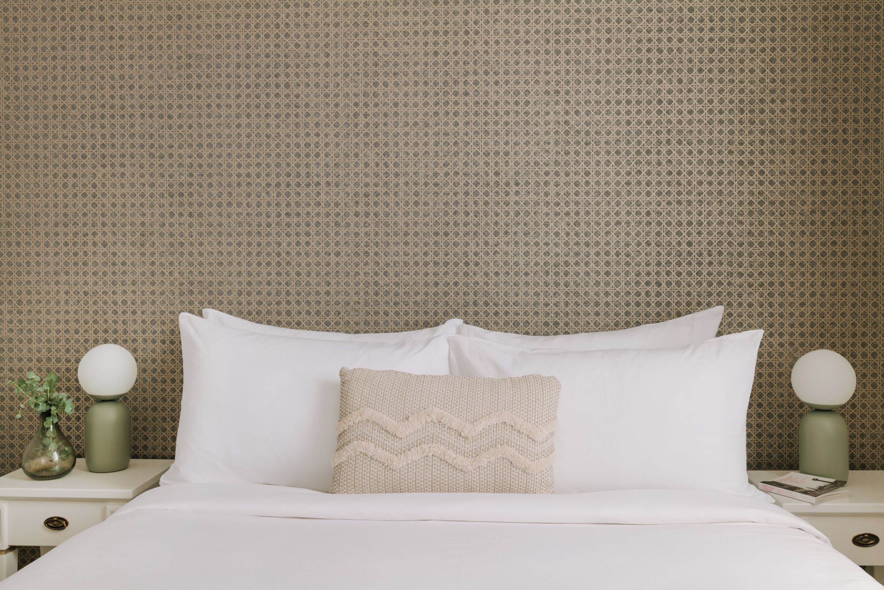 A neatly made bed with white linens and a textured pillow, flanked by two bedside tables with round lamps.