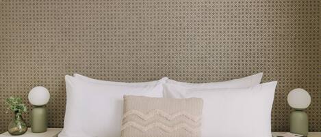 A neatly made bed with white linens and a textured pillow, flanked by two bedside tables with round lamps.