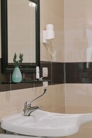 A bathroom with a white sink, a mirror, a towel dispenser, and a hairdryer mounted on the wall.