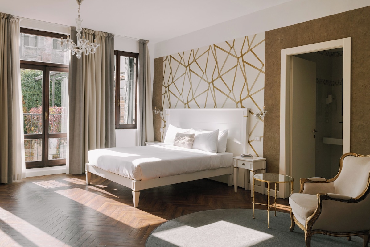 Une chambre moderne avec un grand lit, un lustre, un tapis rond et une vue sur la verdure à l’extérieur.