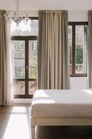 Quarto com cama grande, lustre e vista para a varanda.
