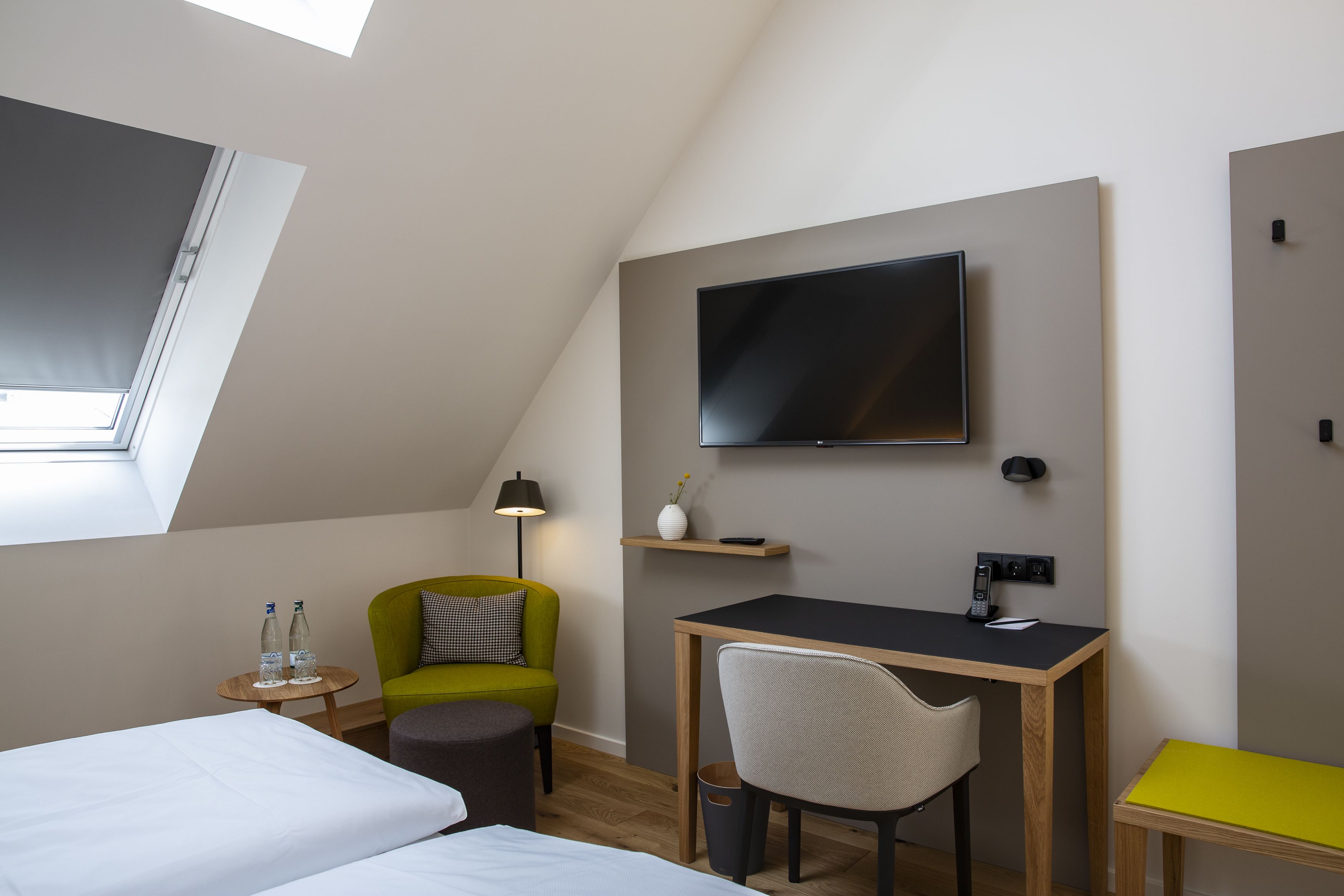 Een moderne hotelkamer met een bed, een bureau, een stoel, een televisie en een tafeltje met waterflesjes.