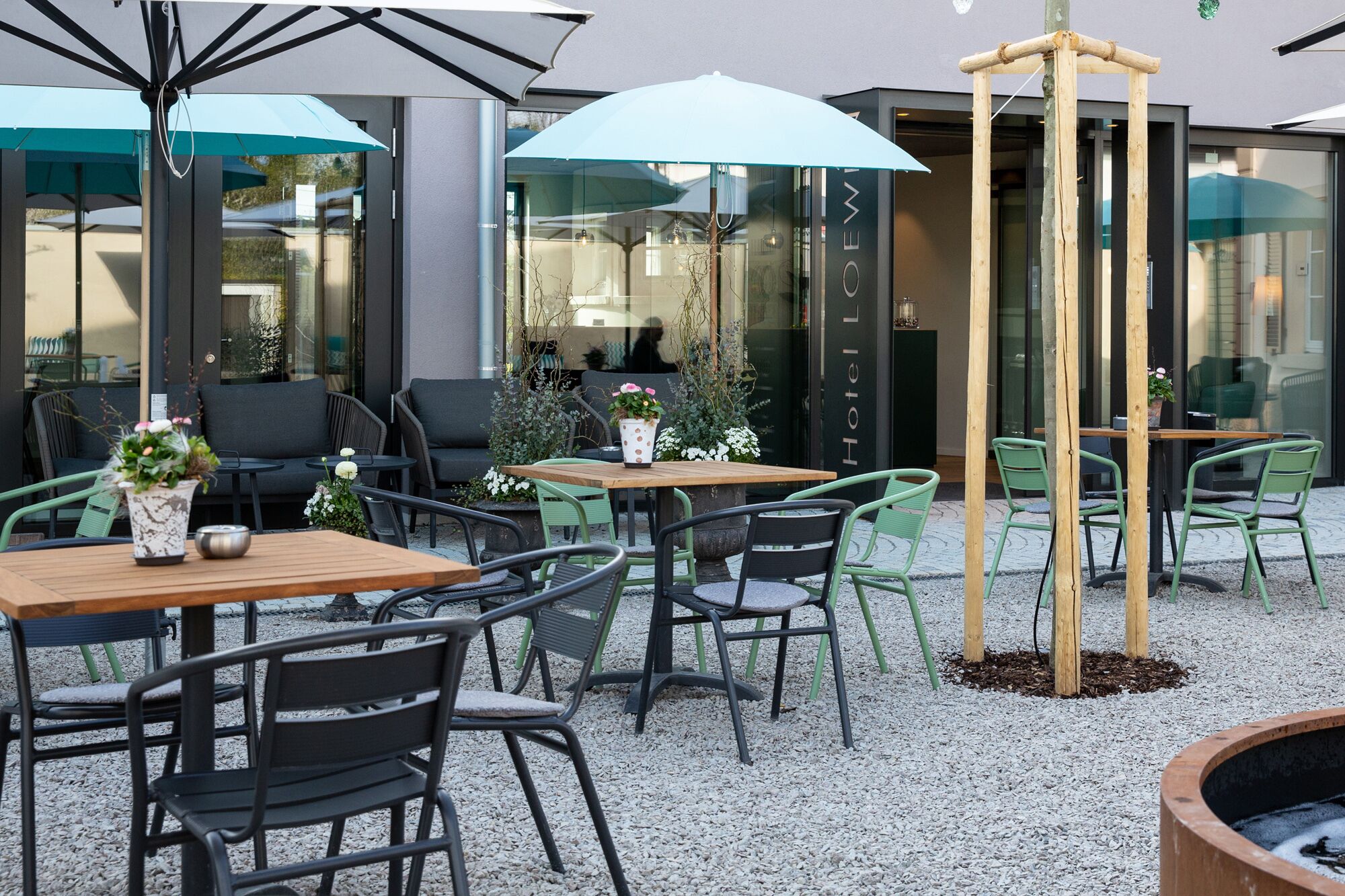 Een buitenzitplaats met tafels, stoelen, parasols en een houten constructie.