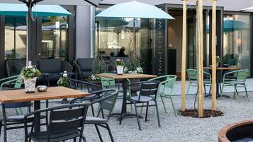 Een buitenzitplaats met tafels, stoelen, parasols en een houten constructie.