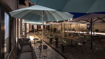 En utomhusplats med sittmöbler, parasoller, möbler av rotting och krukväxter.